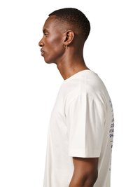 Bočni prikaz muškarca s kratkom kosom i malom naušnicom u obliku prstena koji nosi bijelu majicu s tiskanim tekstom na leđima.