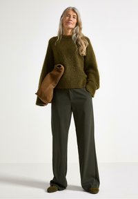 Maglione a maglia verde oliva con vestibilità ampia e tessuto texture, abbinato a pantaloni con gamba larga di un verde scuro e una borsa in camoscio marrone.