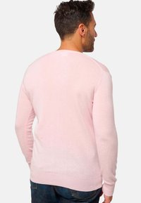 Pull en maille rose clair avec des manches longues, des bords-côtes aux poignets et à l'ourlet, texture visible et finition lisse, porté sur un jean foncé.