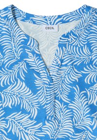 Col de chemise bleu avec motif de feuilles tropicales blanches et une courte patte de boutonnage, avec une étiquette cousue portant le nom de marque Cecil.