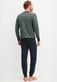 Groene top met patroon en lange mouwen, voorzien van marineblauwe manchetten, gecombineerd met donkerblauwe joggingsbroek. De stof lijkt zacht, met een relaxte pasvorm en taps toelopende broekspijpen.