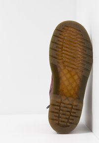 Hnědá gumová podrážka s texturovaným vzorem a vzorovaným motivem; červené svrchní materiály s černými akcenty; detail bočního zipu.