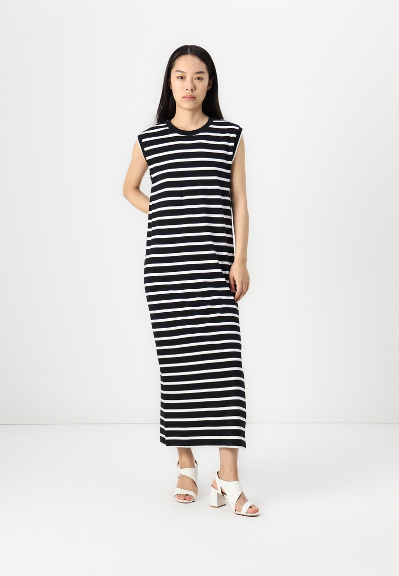 Gestreiftes schwarzes und weißes, ärmelloses Maxikleid mit lockerer Passform. Verfügt über einen runden Halsausschnitt und wird mit weißen Blockabsatzsandalen kombiniert.