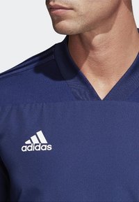 Marinblå idrottströja med V-ringning och strukturerad tyg. Har vitt Adidas-logotyp på vänster sida. Subtila axelband.