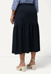 Gonna midi blu navy con un livello inferiore arricciato e vita elastica. Indossata con sandali con tacco a blocco beige chiaro. Tessuto dalla consistenza liscia.