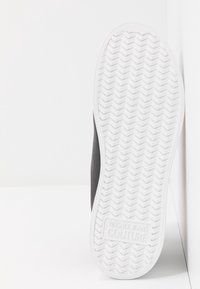 Černá teniska s texturovaným svrškem, bílou gumovou podrážkou, vzorem rybí kosti a vystouplým logem na podrážce. Boční pohled.