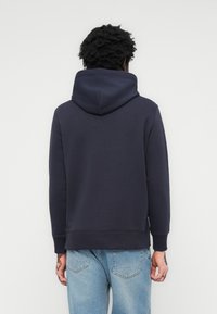 Marineblå hættetrøje med snoretræk i hætten, ribbede manchetter og kant, fremstillet af blødt stof, båret med lyseblå jeans.