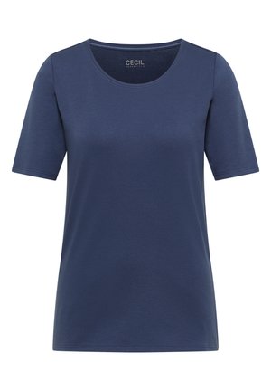 Femme aux longs cheveux bruns porte un t-shirt uni bleu marine à manches courtes, de dos sur un fond clair et neutre.
