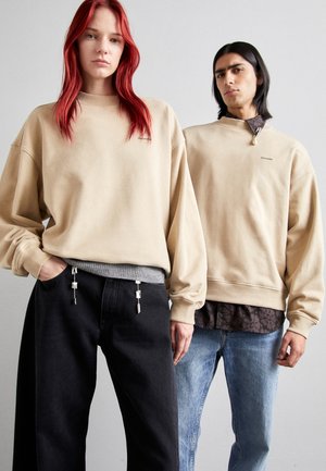 Beige oversized sweatshirts, sorte og denim jeans; detaljer inkluderer sølv hardware og en blomsterprintet skjorte under sweatshirtet.