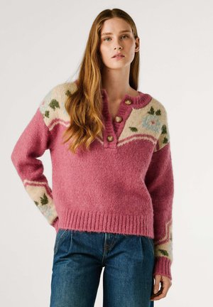 Rosa ulltröja med V-ringning, tre knappar och en krämfärgad yoke med blommönster samt texturerade stickade ärmar. Styler med blå jeans.