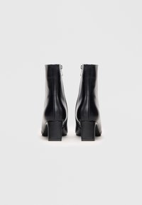 Schwarze Lederstiefeletten mit glatter Oberfläche, quadratischem Absatz und seitlichen Reißverschlüssen. Mit hohem Schaft und minimalistischer Gestaltung.