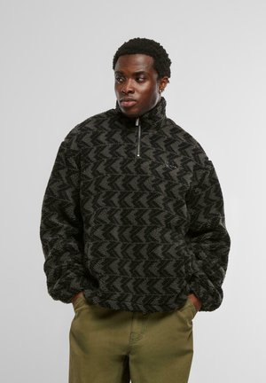 Pullover in fleece con motivo nero e grigio, dotato di un alto colletto e chiusura a metà zip. Presenta una vestibilità comoda con una superficie testurizzata.