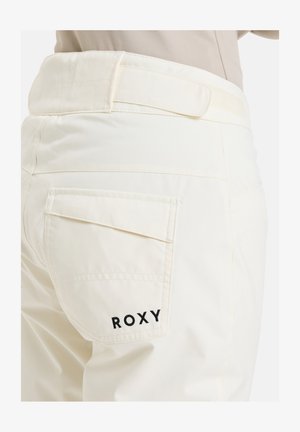 Krémové nohavice s hladkou textúrou, s jednou zadnou vreckom a čiernym vyšitým logom "ROXY" na vrecku.
