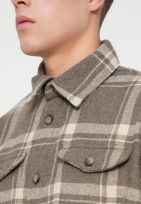 Bruine geruite flanellen shirt met een knoopkraag, twee borstzakken met kleppen en stof van gemiddelde dikte met textuur.