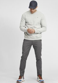 Jasnoszara bluza z okrągłym dekoltem, zestawiona z ciemnoszarymi spodniami w wzory. Sportowe buty z kolorowymi sznurówkami i detalami. Granatowa czapka.