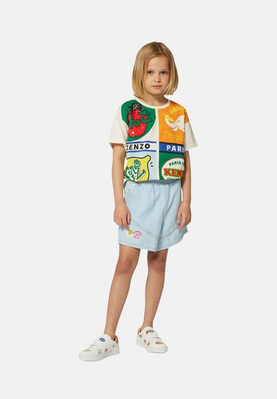 Kleurrijk graphic t-shirt met groene, rode en oranje ontwerpen; lichtblauwe denimrok; witte instapschoenen met veelkleurige patches.
