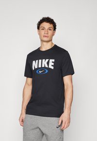 Crna pamučna majica s velikim bijelim ispucalim "NIKE" logom s plavim akcentom. Standardni okrugli izrez i kratki rukavi.