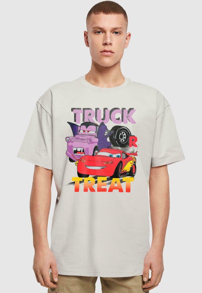 Lys beige oversized t-shirt med et grafisk print af tegneserie-biler med teksten "TRUCK OR TREAT" i kraftige farver. Korte ærmer, lavet af bomuldsmateriale.
