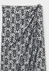 Tissu noir et blanc avec des motifs floraux et géométriques symétriques intricats, partiellement plié pour montrer la texture et le drapé.