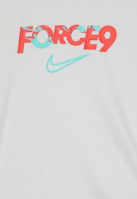 Hvit t-skjorte med rød "FORCE9" tekst med en slitt effekt og en turkise Nike swoosh-logo under. Glatt stoffstruktur.