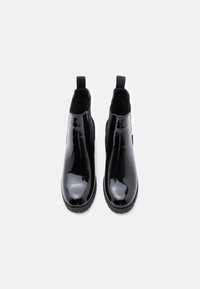 Černé lakované chelsea boty se elastickými bočními panely a poutky. Mají kulatou špičku a texturovanou gumovou podrážku.