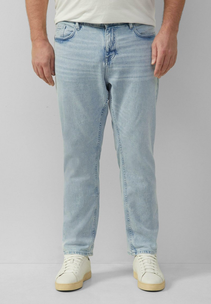 Jeans en denim bleu clair avec une coupe droite, style cinq poches standard et un délavage subtil. Associés à des baskets blanches.