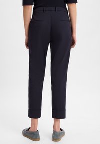 Marineblaue, taillierte Hose mit geradem Schnitt, flachem Bund, zwei Gesäßtaschen und umgeschlagenen Säumen. Glattes Material und minimale Details.