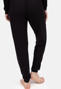 Czarne, luźne spodnie wykonane z miękkiego materiału z elastycznym paskiem w talii, z tapered legs i gładką teksturą.