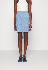 Gonna svasata di un blu chiaro con motivo floreale bianco, con vita elasticizzata, abbinata a sneakers blu scuro con strisce blu chiaro.