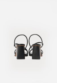 Sandales à talons en cuir noir avec un talon carré, des fines lanières et un design ouvert à l'arrière, présentant une surface lisse et un minimum de détails.
