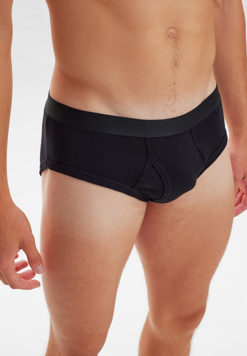 Sorte bomuldsunderbukser med ribbet tekstur og elastisk talje, designet til en tætsiddende pasform med en støttende frontlomme.