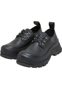Chaussures en cuir noir avec un bout rond, semelle texturée et détails de lacets. Présente de petites anses à l'arrière pour un enfilage facile. Design à semelle épaisse.