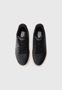 Black athletic shoes with a smooth synthetic upper, lace-up design, perforated detailing for breathability, and a contrasting light sole.