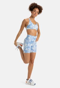 Soutien-gorge de sport floral bleu et shorts taille haute assortis en tissu doux et extensible. Des baskets blanches avec des accents orange complètent la tenue.