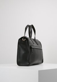 Sort lædertaske med en struktureret design, duale håndtag, en lynlåslomme foran og en glat overflade. Ingen synlige logoer eller udsmykninger.