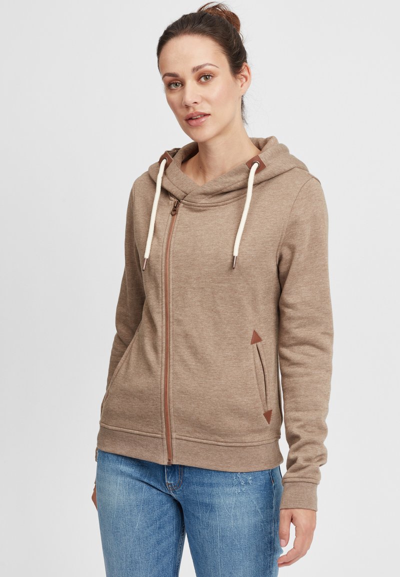 Brun zip-up hette med cowl-neck, kremfargede snorer og faux lærdetaljer. Har sidelommer og et strukturert stoff.