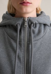Grijze sweatshirt met een hoge kraag en ritssluiting. Voorzien van trekkoordjes bij de capuchon en een glad, gestructureerd materiaal.