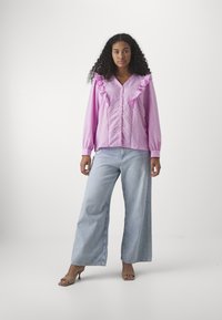 Blusa ruffled rosa chiaro con scollatura a V, chiusura con bottoni e maniche lunghe abbinata a jeans in denim azzurro chiaro a gamba larga e tacchi beige.