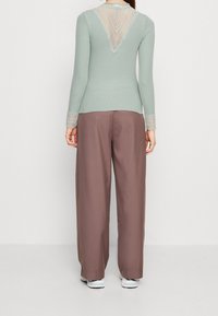 Máte světle mentolový dlouhý rukáv top s krajkovým límcem na zádech a texturovanými rukávy, doplněný hnědými širokými kalhotami a bílými teniskami.