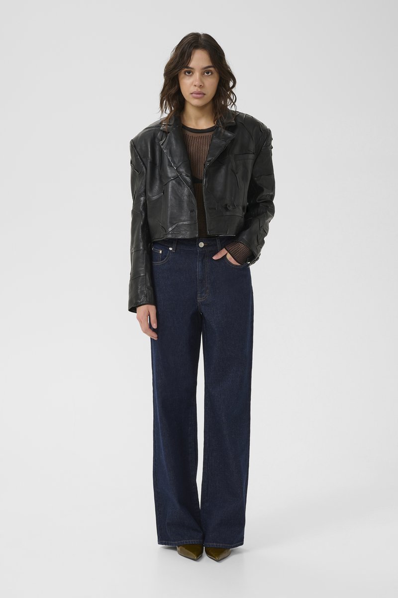 Kortad svart läderjacka med en texturerad yta, i kombination med högmidjade mörkblå vida jeans och olivgröna pumps med spetsig tå.