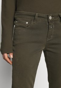 Jean en denim vert olive à coupe droite, doté d'un design à cinq poches, de pièces métalliques argentées et de coutures apparentes.