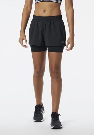 Zwarte sportshorts met een elastische tailleband over strakke zwarte shorts; gecombineerd met zwart-grijze hardloopschoenen.