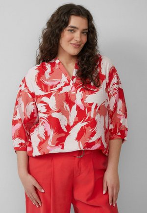 Rood en roze gebloemde blouse met een V-hals, driekwart mouwen en lichte stof, gecombineerd met rode broek met een riem.