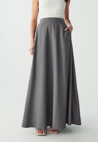 Long gray skirt made from lightweight fabric, featuring a high waistband, side pockets, and a flowing design that drapes to the ankle.