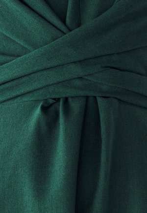 Temnozelena tkanina z mehkobo, ki prikazuje ovit dizajn in vidne gube, ki ustvarjajo globino in volumen.