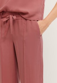 Hosen aus leichtem Rosafarbigen Stoff mit glatter Textur, ausgestattet mit einem elastischen Bund und seitlichen Taschen für eine lässige Passform.