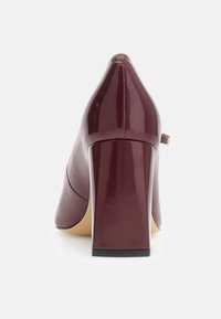 Scarpa con tacco alto in vernice color bordeaux con punta a punta e tacco robusto. Presenta una texture liscia e un piccolo elemento decorativo laterale.