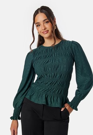 Blusa smock verde scuro con maniche lunghe, tessuto testurizzato, dettagli arricciati in vita e orlo svasato.