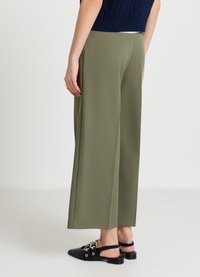 Olivegrüne, weit geschnittene Hosen mit glatter Textur, einem hohen Bund und einer fließenden Silhouette. Kombiniert mit schwarzen, Riemchen-Sandalen.