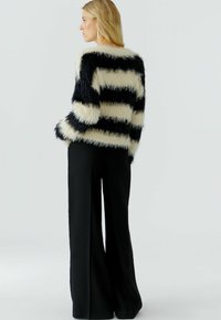 Fuzzy gestreepte trui in zwart en roomkleur met een ruime pasvorm, voorzien van lange mouwen en een ronde hals, gedragen met zwarte broek met wijde pijpen.